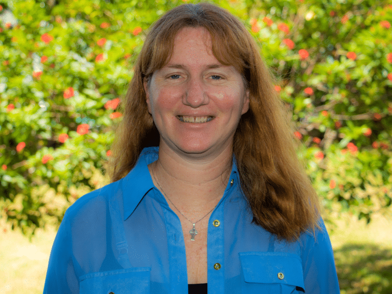 woman in blue shirt smiles with greenery in background